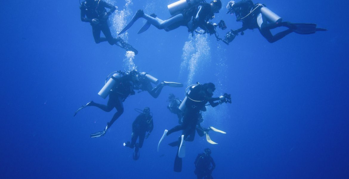 A group of scuba divers descending into infinite blue waters.