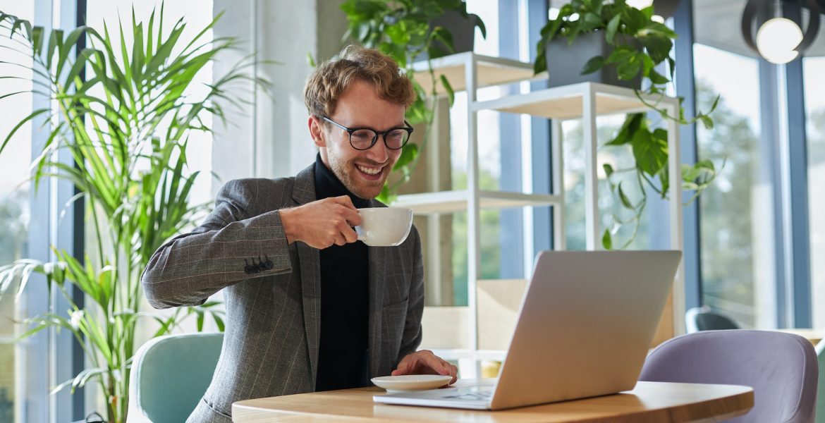 Handsome businessman in formal suit and eyeglasses, with cup of coffee while online call on laptop